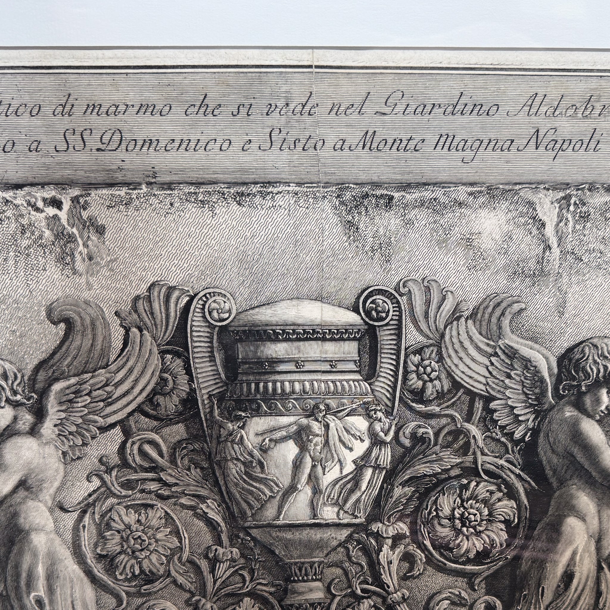 Decorative stone relief with classical figures and floral elements, featuring engraved text.