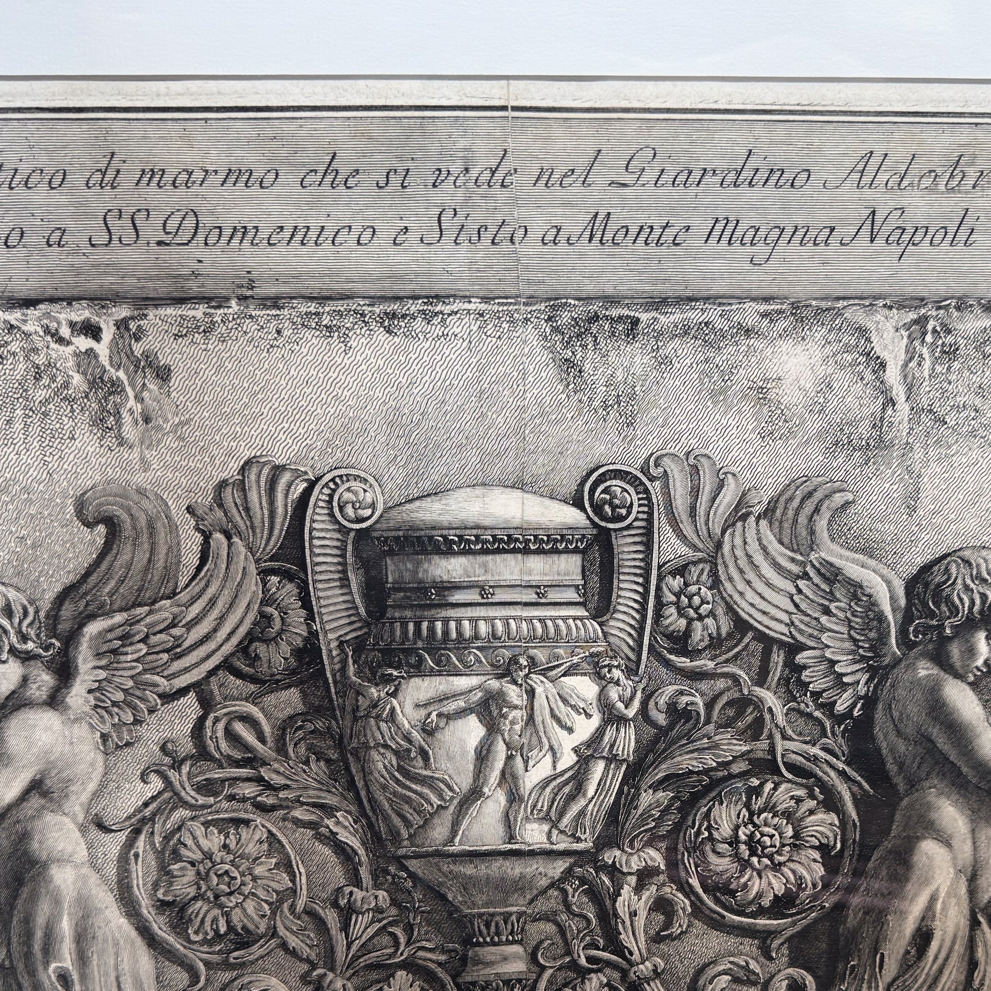 Decorative stone relief with classical figures and floral elements, featuring engraved text.