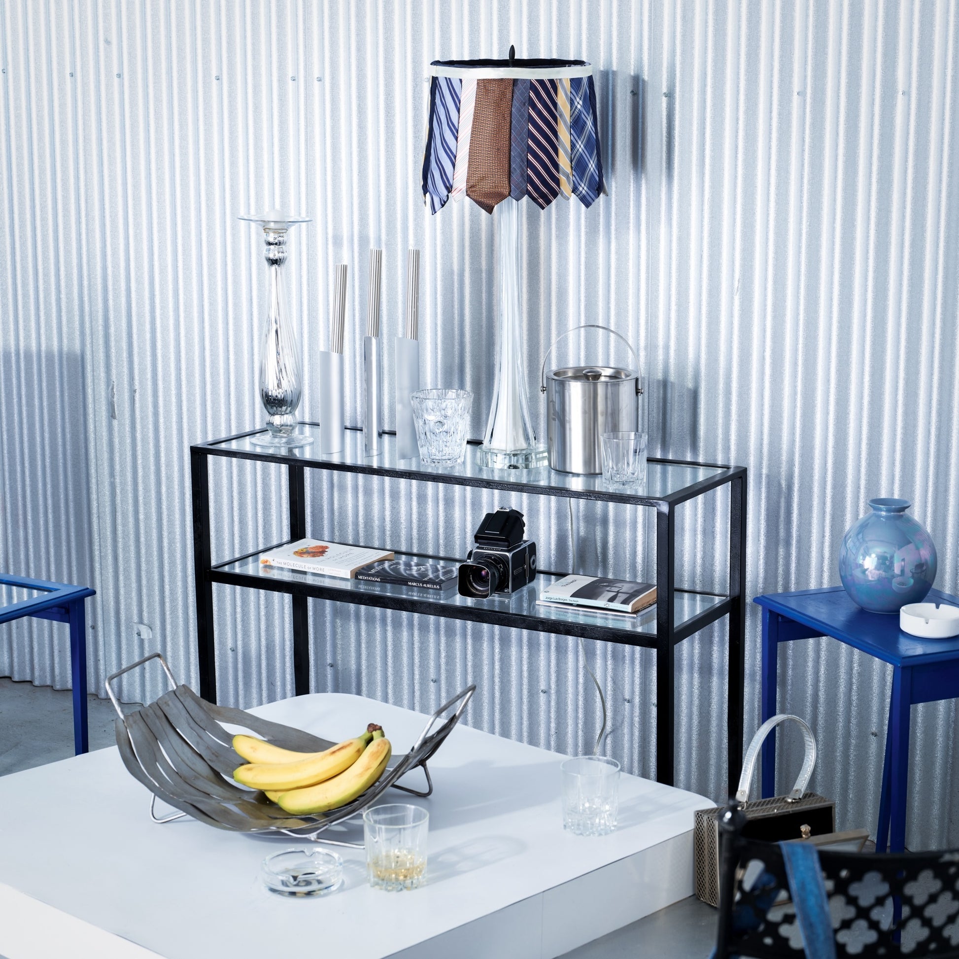 Modern interior with a glass shelf, blue stools, and decorative items against a striped wall.