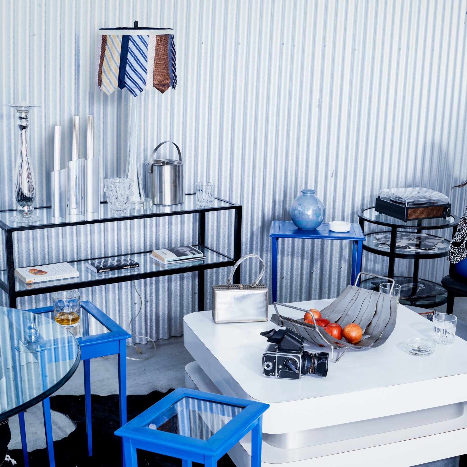 Modern interior with glass tables, blue chairs, and decorative items against a corrugated metal wall.