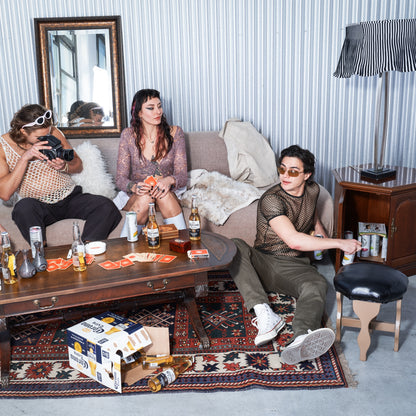 Three people sitting on a couch in a living room with drinks and cards on the coffee table.