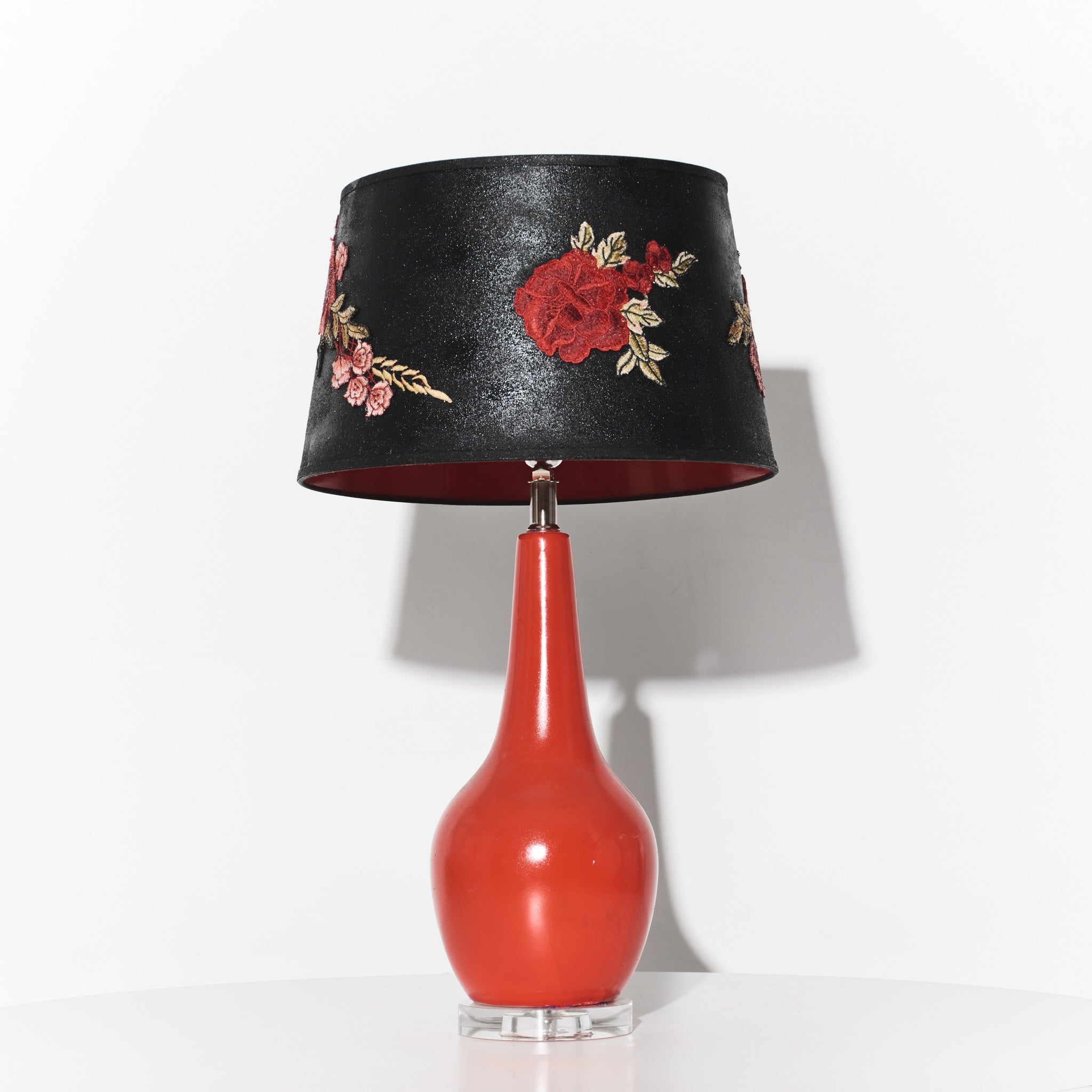 Lamp with a black floral-patterned shade and red base on a white background
