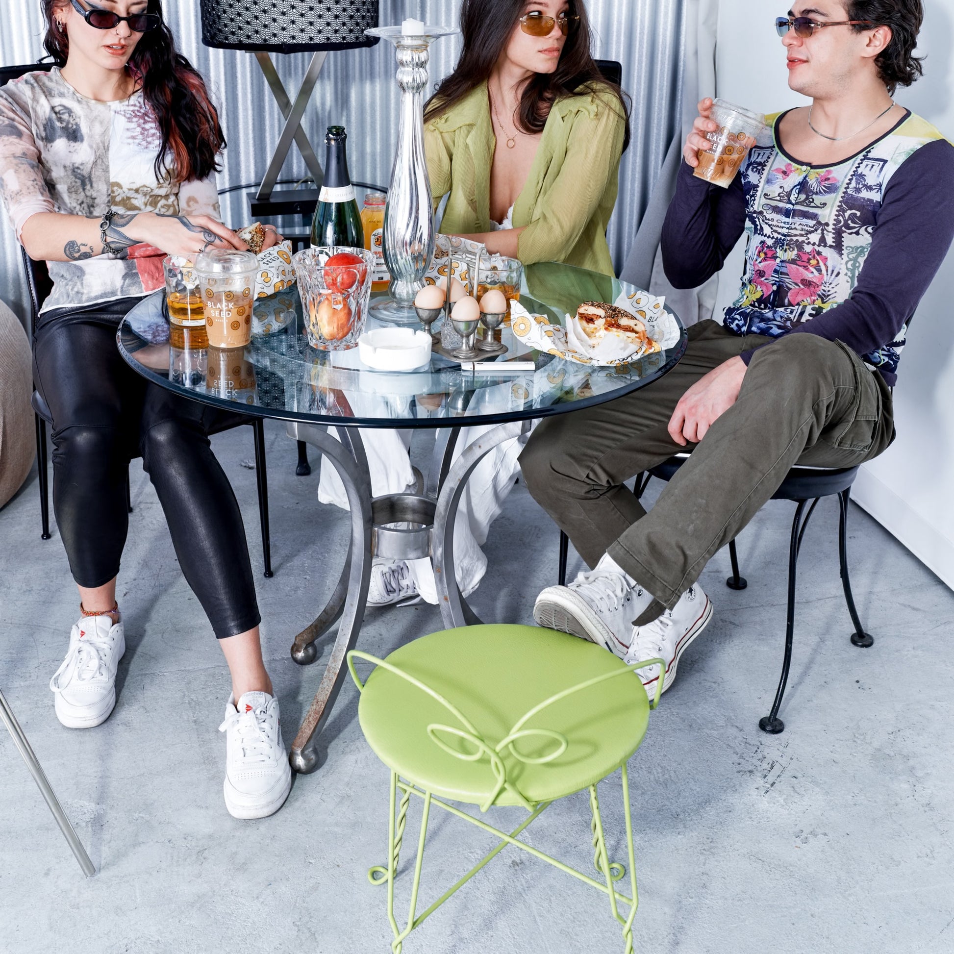 Three people sitting around a glass table with drinks and snacks in an indoor setting.