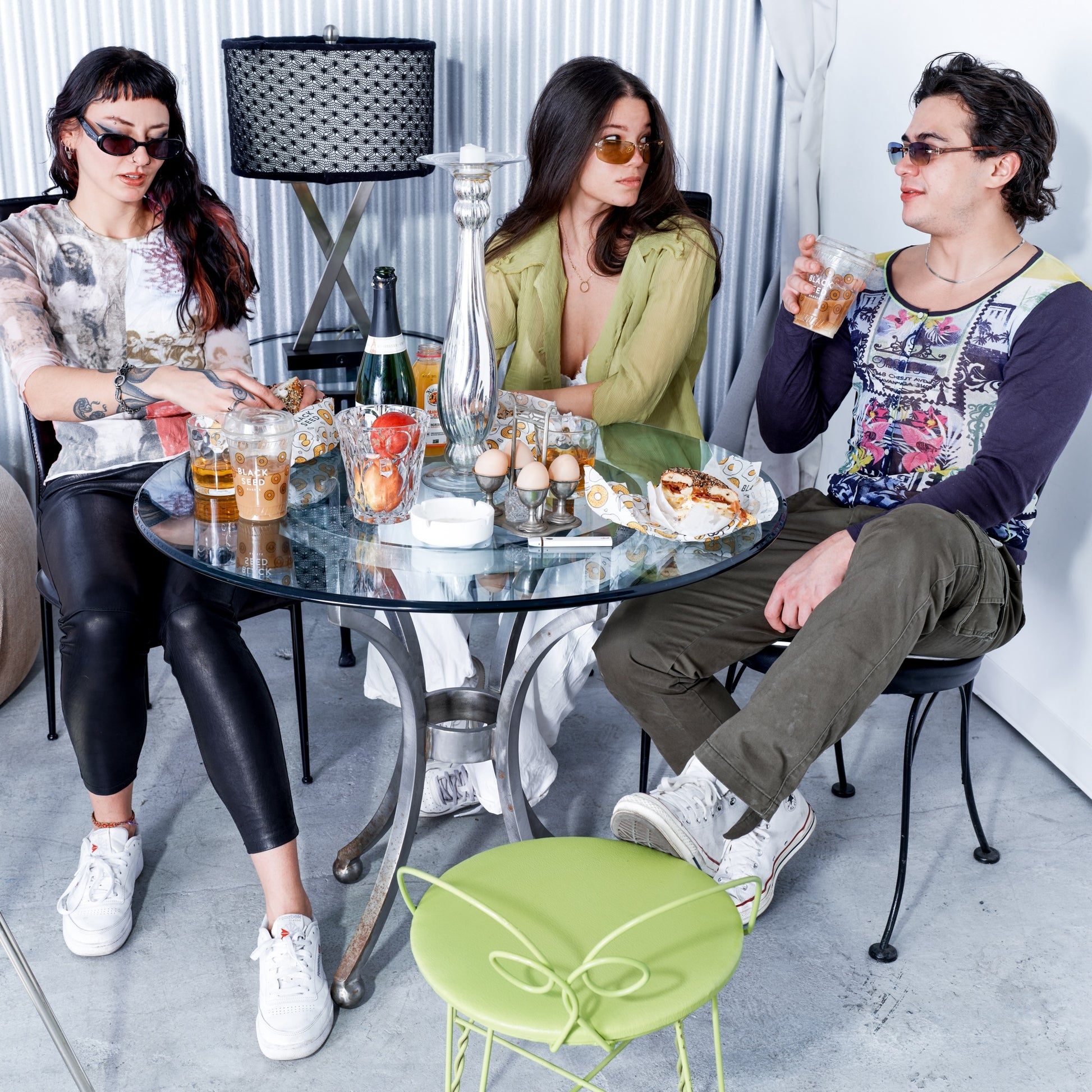 Three people sitting around a glass table with drinks and food in a modern indoor setting.