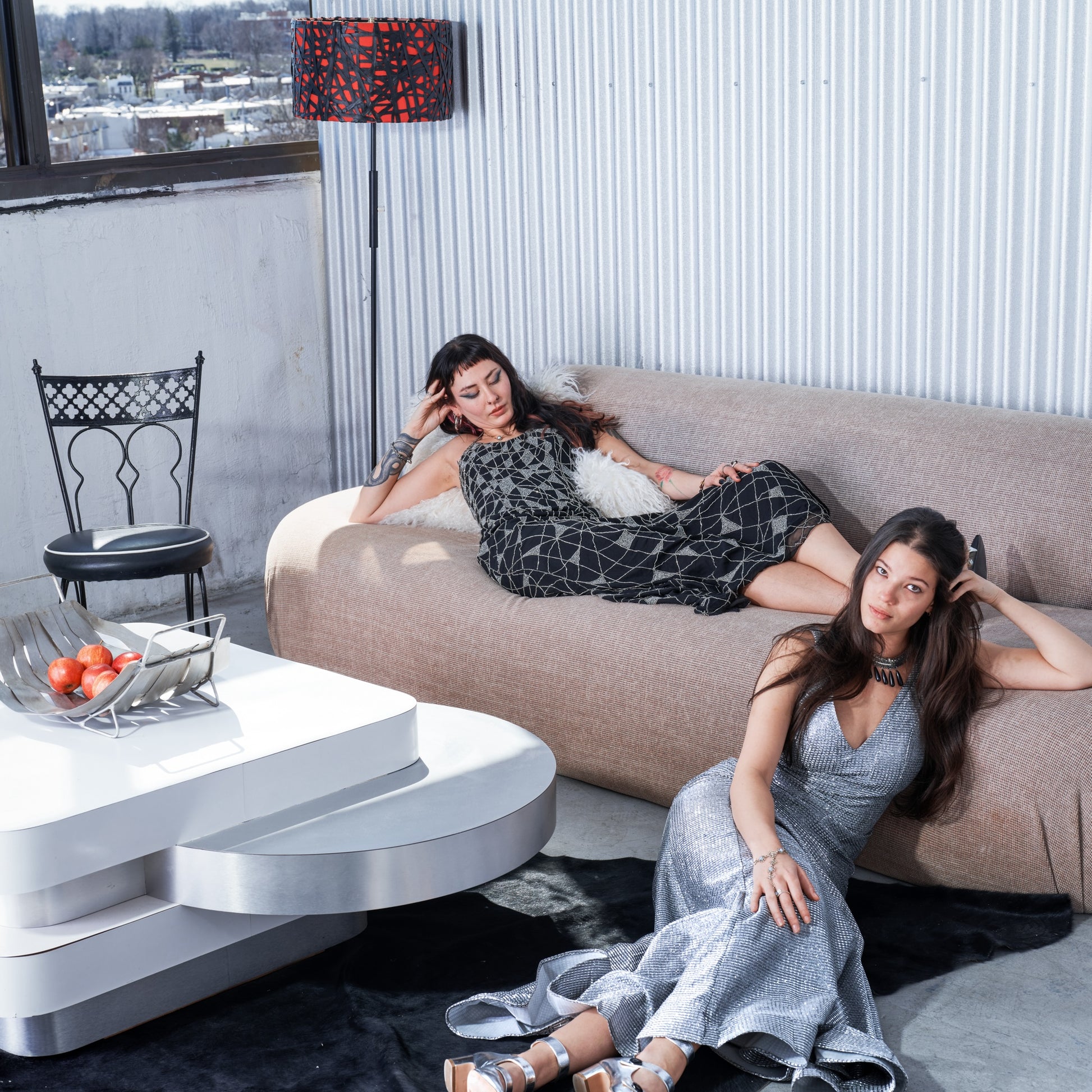 Two women in stylish dresses sitting on a beige sofa in a modern living room.