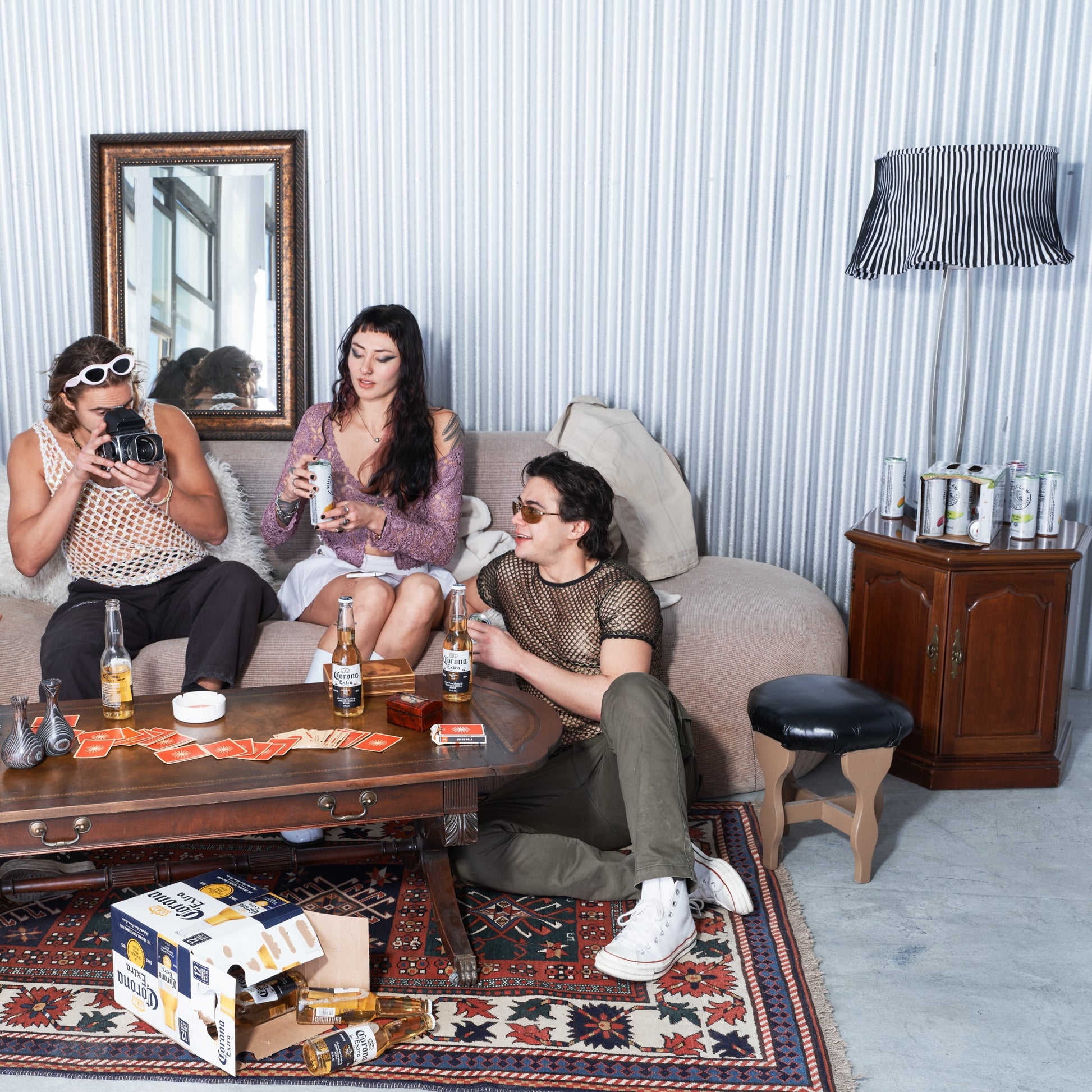 Three people sitting on a couch in a room with a mirror, lamp, and various items on a table.