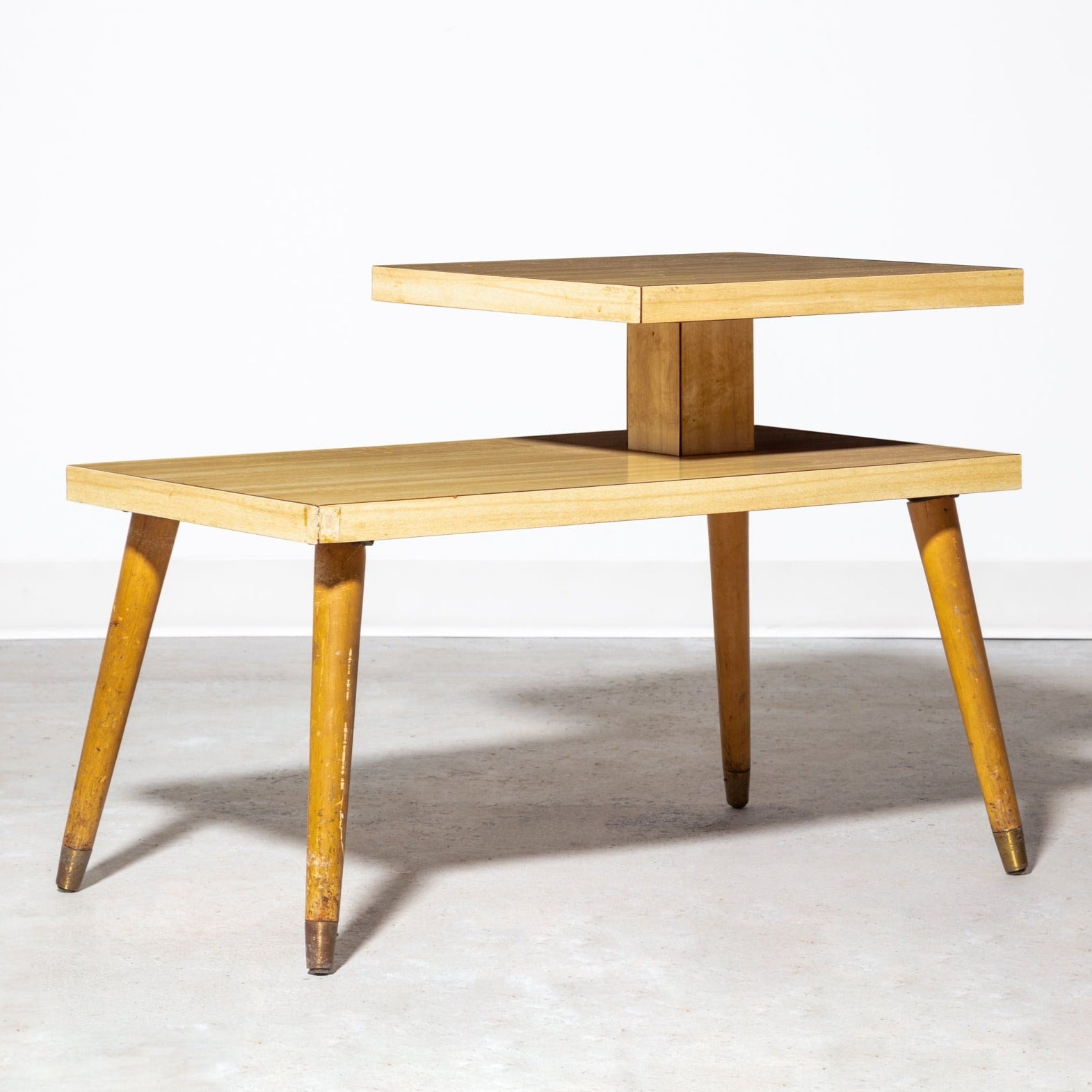 Vintage mid-century modern step end table, designed with smooth wood grain and splayed, tapered legs with brass end caps