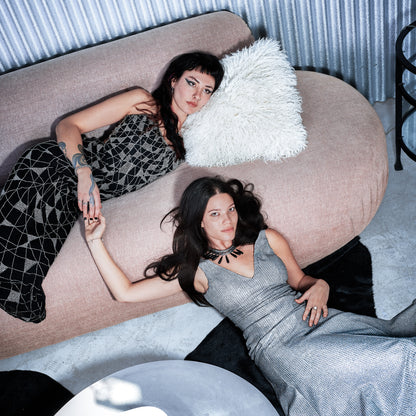 Two women lying on a pink couch with a white pillow.