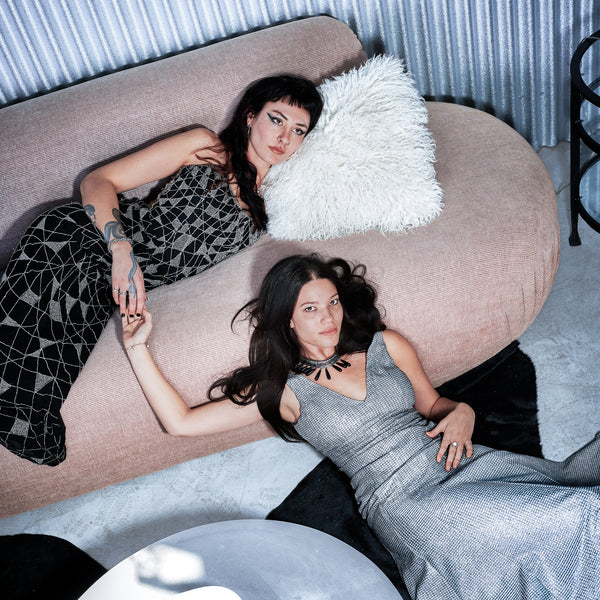 Two women lying on a pink couch with a white pillow.