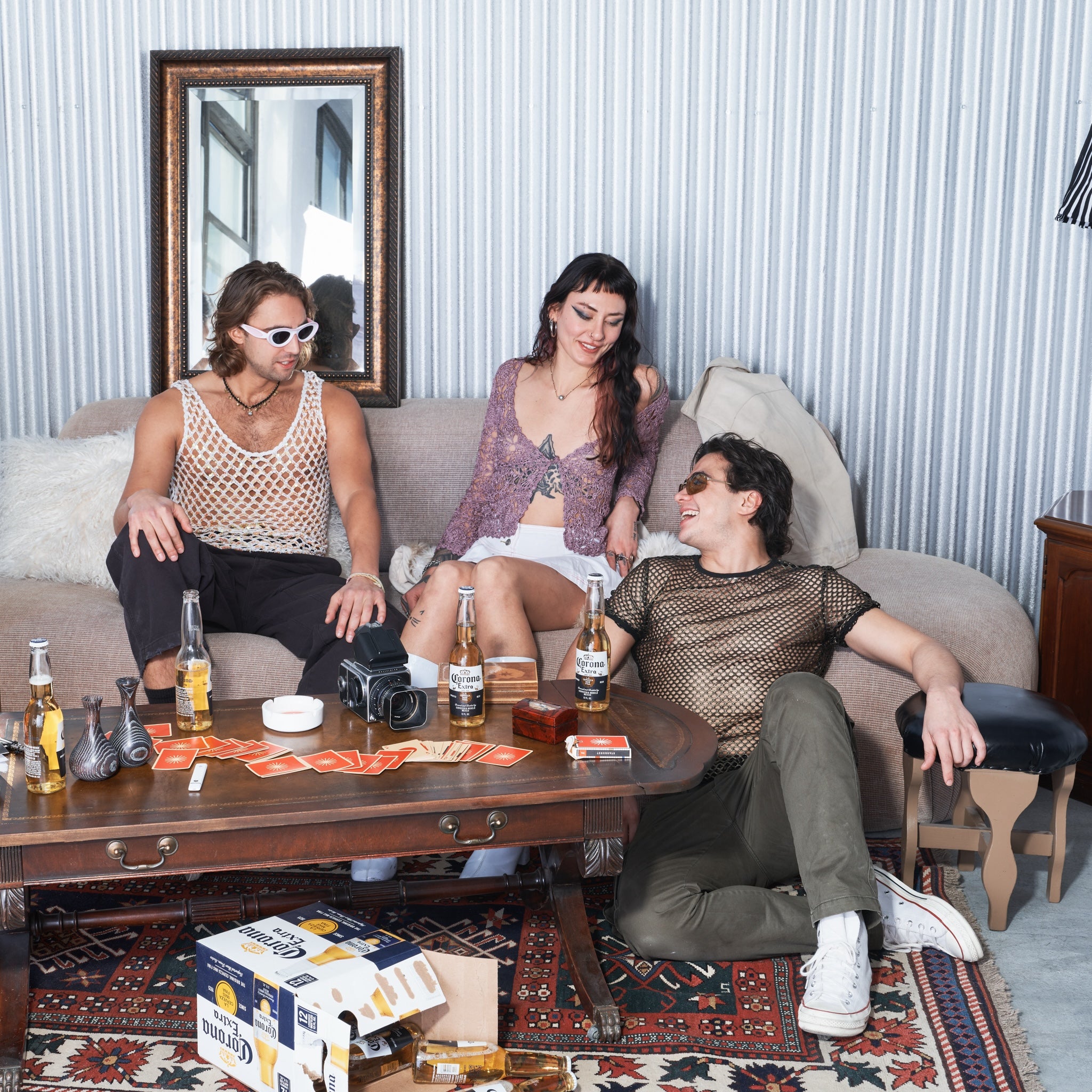 Three people sitting on a couch in a living room with drinks and snacks.