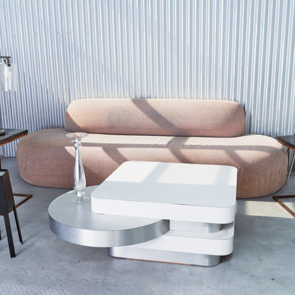 Modern beige sofa with a white and silver coffee table in a room with striped wallpaper.